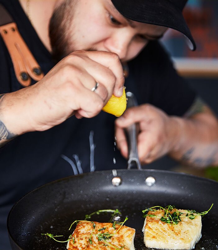Koch bereitet Seelachs in einer Pfanne zu
